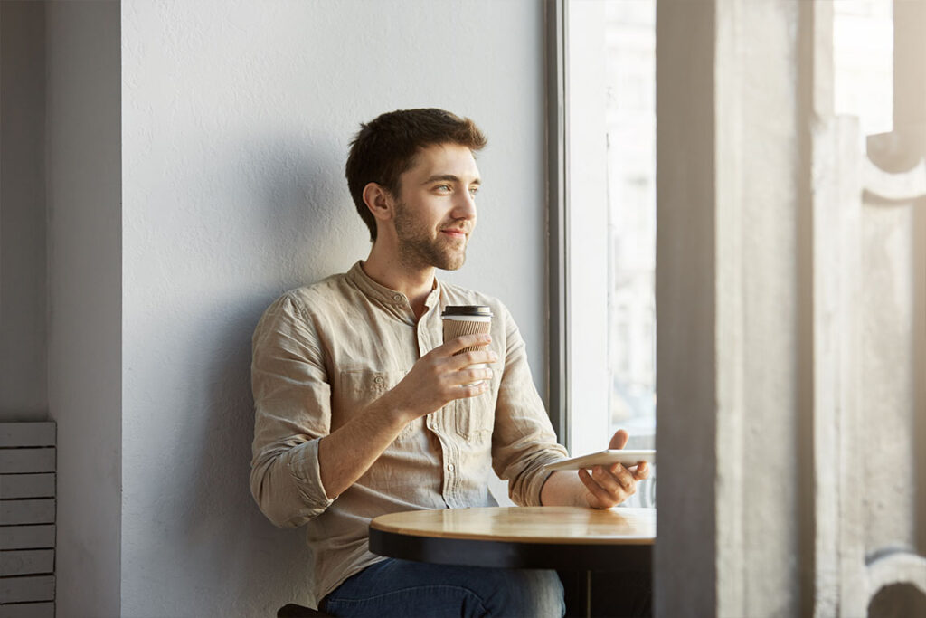 man holding coffee cup looking out window